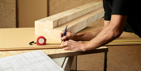 Worker marking wood with pencil, tape measure