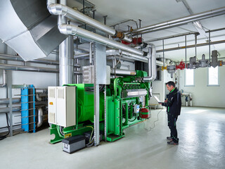 Combined heat and power plant, worker using laptop in front of gas engine
