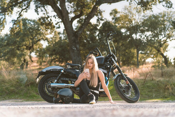 Blond female biker using smart phone while sitting against motorcycle on roadside