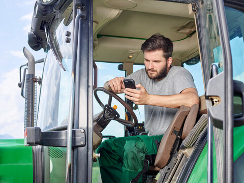 Farmer sitting on tractor using cell phone