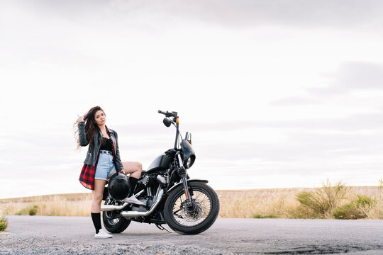 Young Female Biker Standing On Road With Motorbike