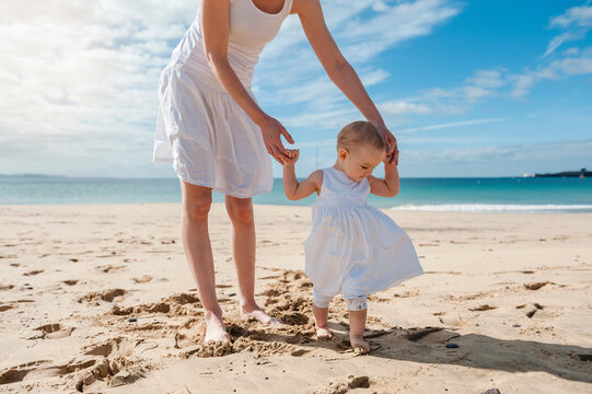Mother helping little daughter walking on the beach