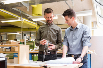 Two smiling men with plan looking at product in factory