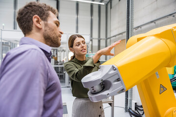 Businessman and woman having a meeting in front of industrial robots in a high tech company