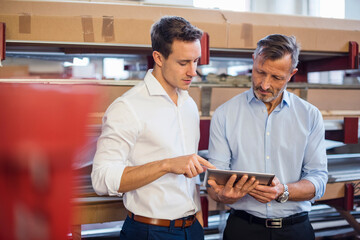 Two businessmen in factory storeroom looking at tablet