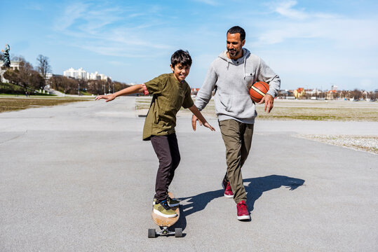 Father and son with longboard and basketball outdoors