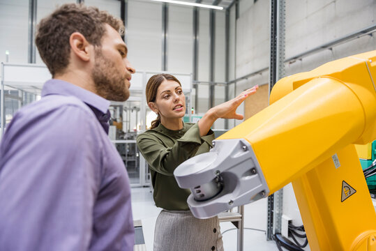 Businessman and woman having a meeting in front of industrial robots in a high tech company