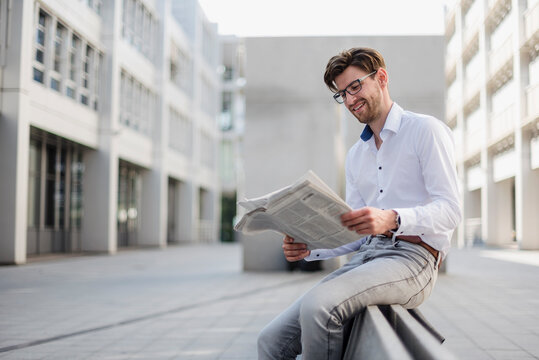 Smiling businessman sitting in the city reading newspaper
