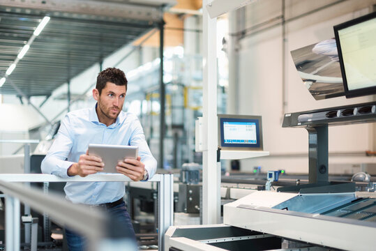 Businessman with tablet looking at machine in modern factory