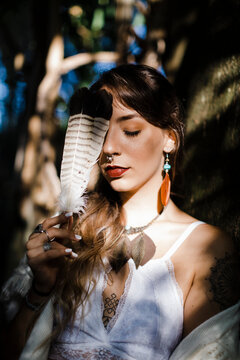 Woman covering face with feather while leaning on tree