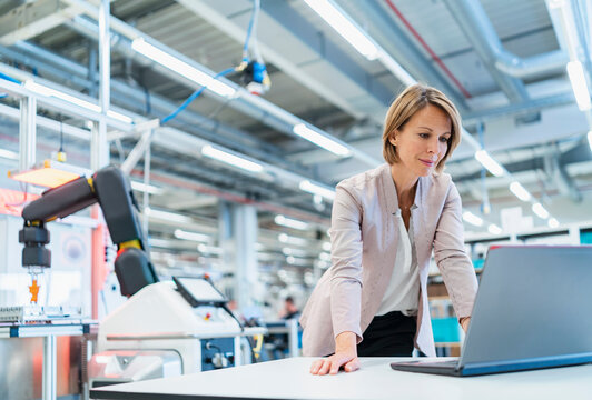 Businesswoman in a modern factory hall using laptop