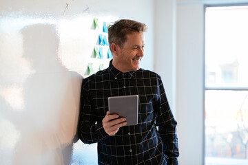 Smiling businessman with tablet in office leaning against whiteboard