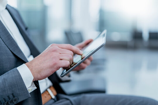 Close-upof businessman sitting in waiting area using tablet