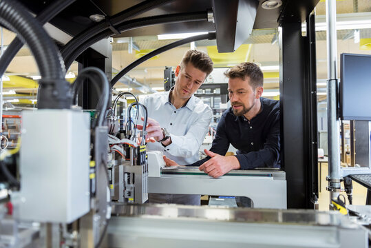 Two men examining machine in factory
