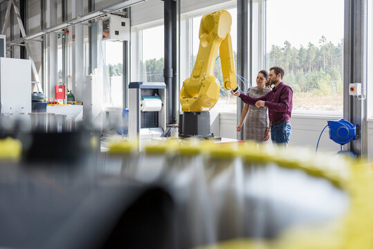 Businessman and woman having a meeting in front of industrial robots in a high tech company