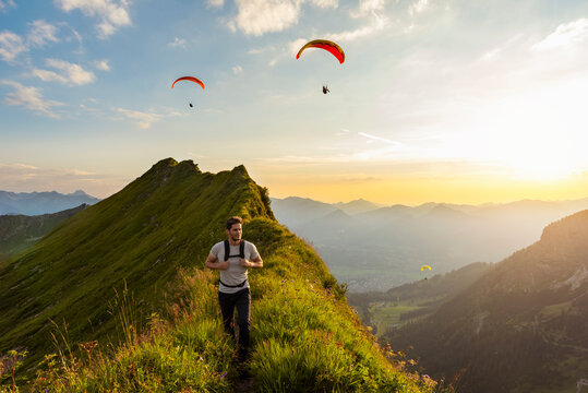 Germany, Bavaria, Oberstdorf, man on a hike in the mountains at sunset with paraglider in background