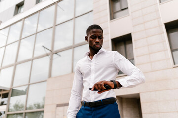 Male entrepreneur checking time on wristwatch while standing against office building in city