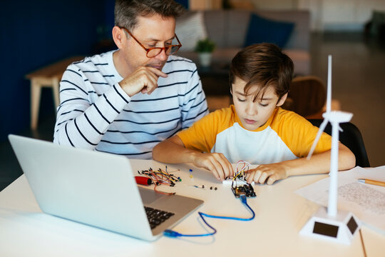 Father and son assembling a construction kit with laptop and wind turbine model