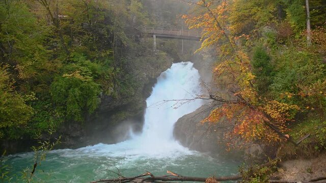 Raging waterfall in pristine nature, Vintgar gorge, Slovenia. Famous bridge over river Radovna. Colorful autumn landscape. Static shot, real time, wide angle