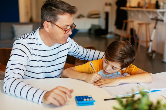 Father watching son doing homework at table