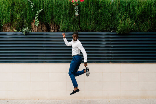 Male professional jumping on sidewalk against surrounding wall in city
