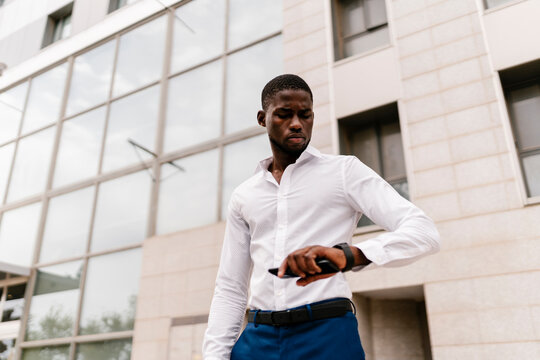 Male entrepreneur checking time on wristwatch while standing against office building in city