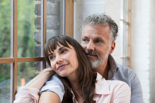 Mature couple sitting on window sill, looking out of window