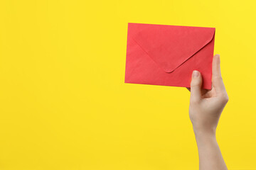 Woman holding red paper envelope on yellow background, closeup. Space for text