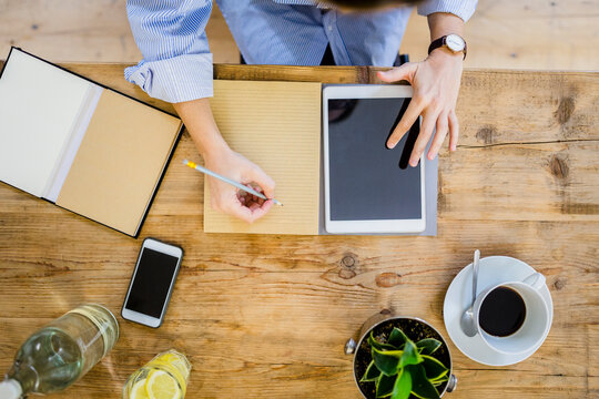 Top view of woman at wooden desk with notebook, cell phone and tablet