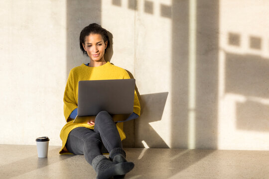 Portrait of smiling young woman sitting on the floor using laptop - Powered by Adobe
