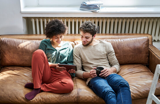 Young man and young woman sitting on couch with cup of coffee and tablet