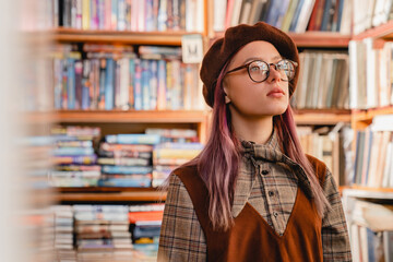 Dreamy thoughtful caucasian young hipster girl in glasses standing in the library or bookshop