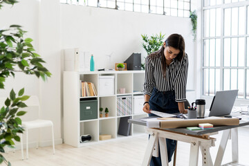 Young female design professional examining plan at desk while working in creative office