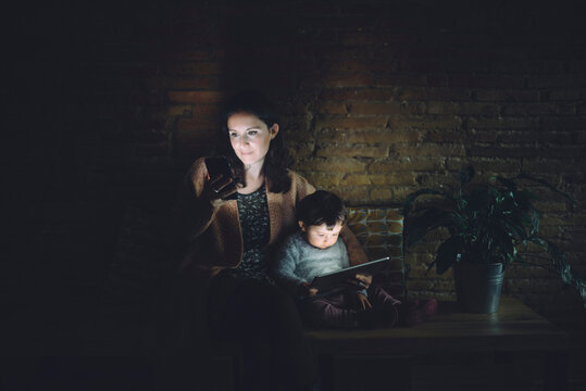 Mother and daughter using cell phone and digital tablet at home in the dark