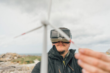 France, Brittany, Meneham, man with miniature wind turbine wearing VR glasses at the coast