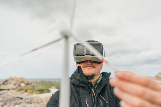 France, Brittany, Meneham, man with miniature wind turbine wearing VR glasses at the coast