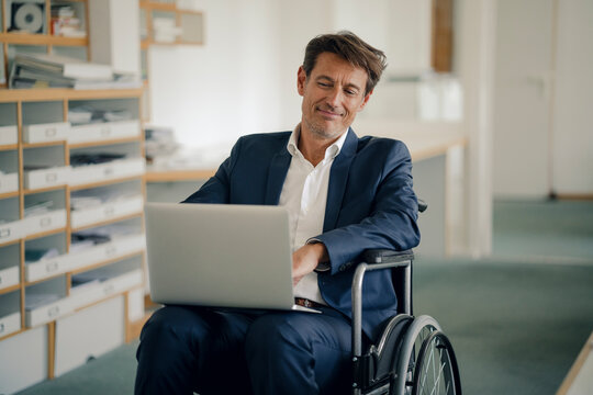 Businessman in wheelchair, using laptop in office