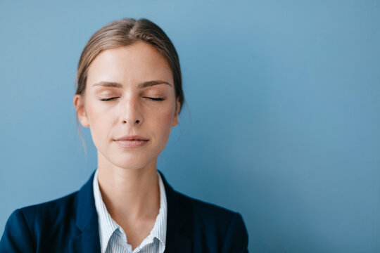 Portrait of a young businesswoman against blue background, relaxing with eyes closed