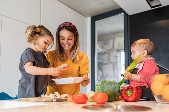 Mother and girl preparing food while baby daughter sitting on kitchen island