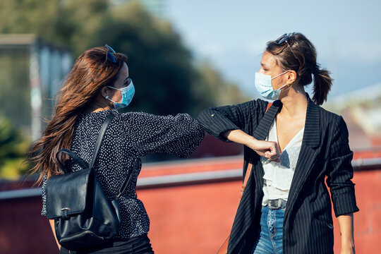 Friends wearing face mask giving elbow bumps while standing in city