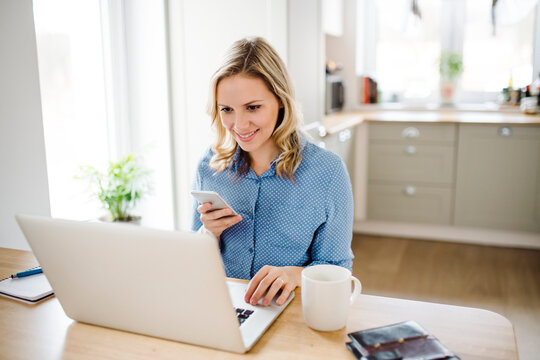 Smiling woman with laptop and cell phone working at home