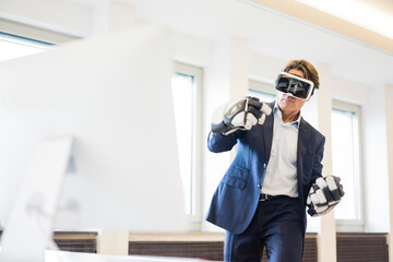 Businessman wearing VR glasses and ice hockey gloves in office