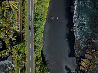 Indonesia, Bali, Aerial view of men skateboarding on asphalt road stretching along black coastal beach