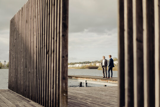 Two businessmen standing on jetty at a lake talking