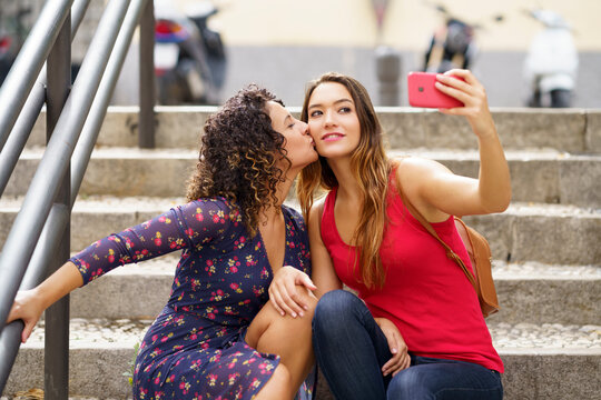 Lesbian couple taking selfie while sitting on staircase in city
