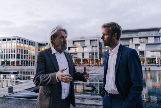 Two businessmen talking at city harbor at dusk