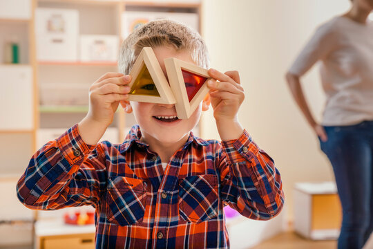 Boy holding wooden and colorful blocks before his eyes in kindergarten