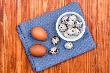Quail eggs in white ceramic bowl on blue kitchen cloth. Top view. Detailed closeup of spotted quail eggs, rustic wooden background