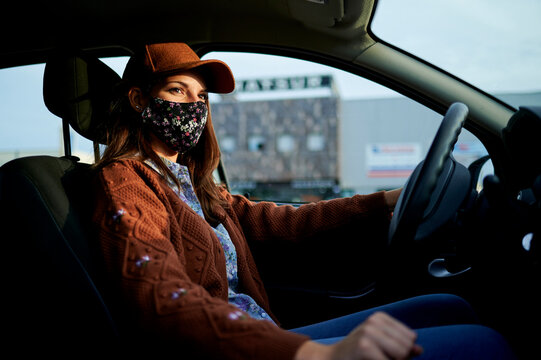 Young woman with cap and face mask driving car in city