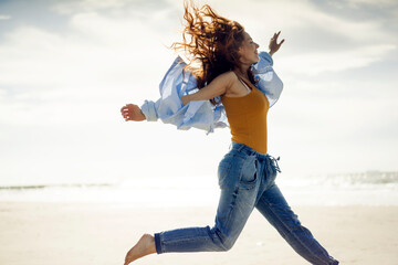 Happy woman having fun at the beach, jumping in the air